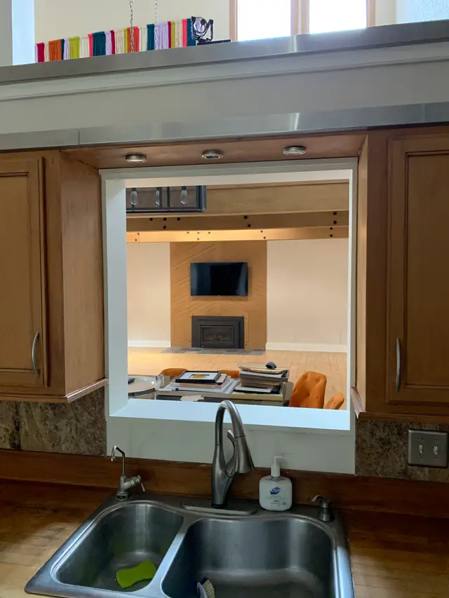 A custom kitchen pass through window opened into a living room with a fireplace